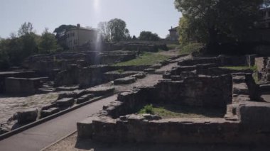 Arka planda ağaçlar olan antik taş kalıntıları, açık hava ortamında parlak güneş ışığı altında yakalandılar..