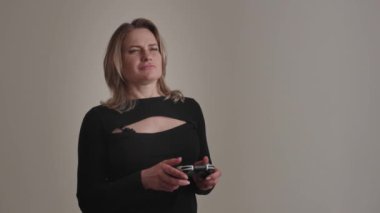 Günlük kıyafetli bir kadın, izole edilmiş bir arka plana karşı kontrolörlü bir video oyunu oynamakla derinden meşguldür.