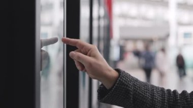 Halka açık bir yerde dijital ekrana dokunan bir elin yakın görüntüsü, modern teknolojiyi vurguluyor.