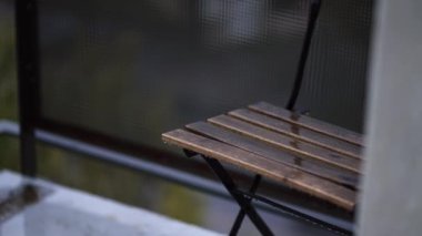Yağmurlu bir günde arka planı bulanık, balkonda ıslak ahşap bir sandalye huzurlu bir atmosfer yaratıyor.
