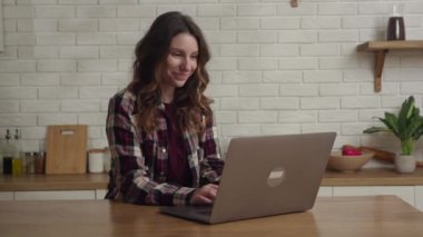 Modern bir mutfakta dizüstü bilgisayar kullanan gülümseyen bir kadın, teknoloji, yaşam tarzı veya ev temaları için uygun.