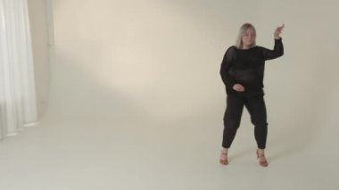 Şık ve şık giyinmiş bir kadın zarif, modern, minimalist bir stüdyo odasında dans eder.