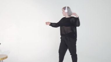 Zarif siyah elbiseli şık bir dansçı, parlak bir stüdyoda kulaklık takarken zarifçe hareket eder.