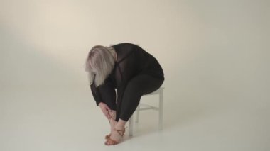 Sandalyeye oturmuş, şık ayakkabılarını modern, minimalist moda ortamında ayarlayan bir insan.