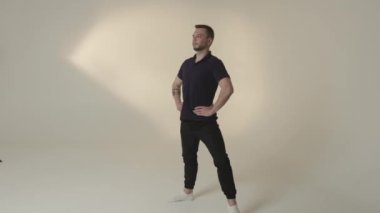 Genç bir adam minimalist bir stüdyo ortamında kendine güvenerek poz veriyor, gerçek sanatın vücut bulmuş hali.