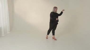 Minimalist bir stüdyoda, kendine güvenen bir kadın kendine has tarzını ve zarafetini sergileyerek sert bir poz verir.