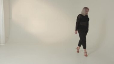 Profesyonel bir manken minimalist bir stüdyoda yürürken kendine güvenen şık bir kıyafet sergiler.