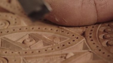 Oymalı bir alet kullanarak, ahşap üzerine karmaşık desenler oyan bir elin yakın çekimi..