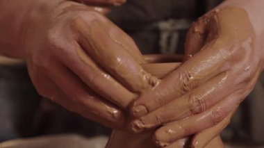 Çamur tenceresini şekillendiren bir çömlekçinin elleri, yaratılış sürecinde yeteneğini ve sanatını sergiliyor.