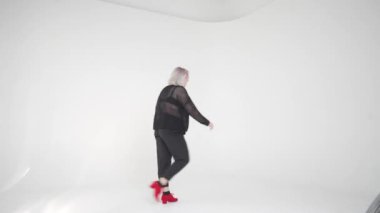 Zarif ve şık giyinmiş bir kadın zarif bir şekilde dans eder. Parlak ve minimalist bir stüdyo ortamında.