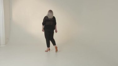 Şık giyimli bir kadın minimalist bir stüdyo ortamında kendine has yeteneğini sergiliyor.