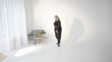 Şık bir kadın, yumuşak mobilyalarla dolu parlak, minimalist bir stüdyoda özgüvenle ve zarafetle duruyor.