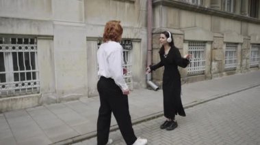 Bir erkek ve bir kadın, her ikisi de kulaklık takmış, kalabalık bir kaldırımda neşeyle dans ediyorlar. Video onların enerjisini yakinlarinda iki kadinin konusmasiyla yaklasiyor, hareketli atmosferi ve toplum bilincini gelistiriyor.