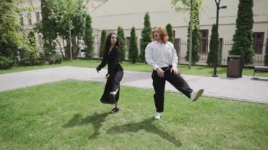 Huzurlu bir parkta, iki kadın çimlerin üzerinde birbirlerine bağlanır, samimi bir şekilde sohbet ederler. Yakınlarda, birkaç dans, neşe ve birlikteliğin somutlaşması.