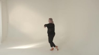 Zarif ve zarif bir şahsiyet ışıkla dolu, parlak ve minimalist bir stüdyoda zarif bir şekilde dans ediyor.