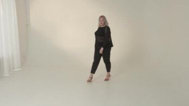 Parlak bir stüdyoda, şık giyinmiş kendine güvenen bir kadın zarif moda anlayışını sergiliyor.