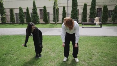Videoda çimlerin üzerinde dans eden iki kadının olduğu canlı bir park gösteriliyor. Bir erkek ve bir kadın, eğlenceye katılıyor ve zarif hareketler sergiliyor.