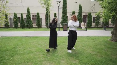 Bu ilgi çekici video parkta iki kadını takip ediyor, zarif siyah elbiseler içinde yürürken ve dans ederken neşeli sohbetler ediyorlar, doğallığı kucaklıyorlar.
