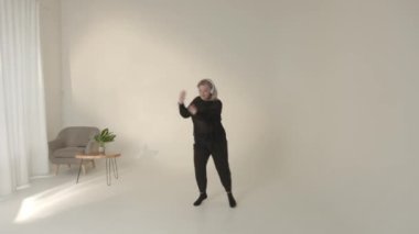 Bir insan doğal ışıkla dolu, parlak, minimalist bir stüdyoda anlamlı ve tutkulu bir şekilde dans ediyor.