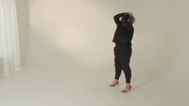 Şık, siyah bir kıyafet giymiş şık ve şık bir kadın modern, minimalist bir stüdyoda zarif bir poz veriyor.