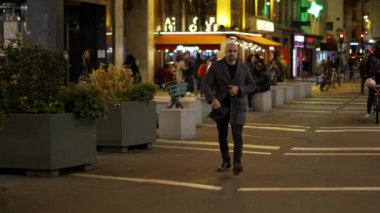 Bir adam, neon ışıkları, hareketli sokaklar ve canlı bir şehir atmosferiyle, gece canlı bir şehirde geziniyor.