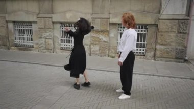 Canlı bir sokak sahnesinde, bir adam ve bir kadın kaldırımda neşeyle dans ederken, iki kadın yakınlarda sohbet ederken, bağlantı ve kutlamaları yansıtıyor.