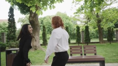 Canlı bir parkta, iki kadın neşeyle dans eder, dostluk ve bağ gösterirler. Yakınlarda, birkaç sohbet, sosyal ortamı geliştirmek.