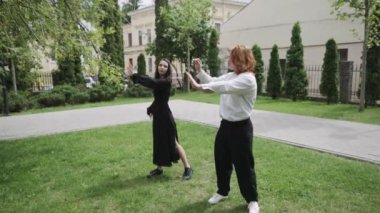 Canlı bir parkta, bir erkek ve bir kadın neşeyle dans ederken, yakınlarda, iki kadın gülüyor ve çimenlerin üzerinde birbirlerine eşlik etmekten zevk alıyorlar.