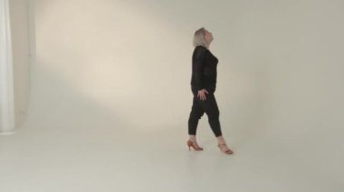 Kendine güvenen bir kadın minimalist bir stüdyo ortamında zarif bir şekilde yürürken zarafetini sergiler.