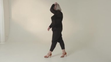 Şık bir model zarif bir şekilde şık siyah bir elbise sergiliyor. Minimalist bir stüdyo ortamında çarpıcı topuklularla eşleştirilmiş.