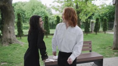 In a serene park, a man and woman have a lighthearted talk on a bench while two women share camaraderie nearby, creating a warm atmosphere