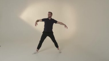Yetenekli bir erkek dansçı, parlak, minimalist stüdyo ortamında etkileyici ve sanatsal bir poz sergiliyor.