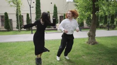 Yürek ısıtan bir video, güneşli bir parkta neşeyle dans eden iki kadını gösteriyor, arkadaşlığı somutlaştıran. Bir adam onlara katılır, pozitifliği arttırır.