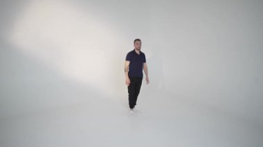 Bir adam, parlak ve minimalist bir stüdyo ortamında, modern yaşam tarzını göstererek güvenle yürür.