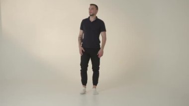 Modayı takip eden bir adam, rahat tavırlı, modaya uygun giyinen, minimal bir stüdyoda kendine güvenerek duruyor.
