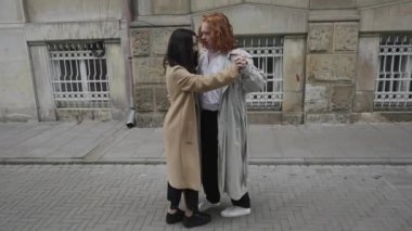 Canlı bir şehirde, trençkotlu kendine güvenen bir kadın sıcak bir kucaklaşmayla arkadaşını selamlar. Neşeli zamanları, şehir yaşamının ortasındaki dostluğu vurguluyor.