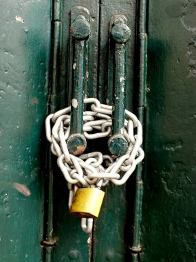 Yeşil paslı kapı, metal zincir ve altın asma kilit ile kilitlenmiş. Gayrimenkul ve İş Güvenliği kavramı.