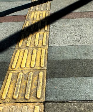 Kör yaya için kabartmalı sarı asfalt üzerinde uzun bir gölgenin soyut arkaplanı..