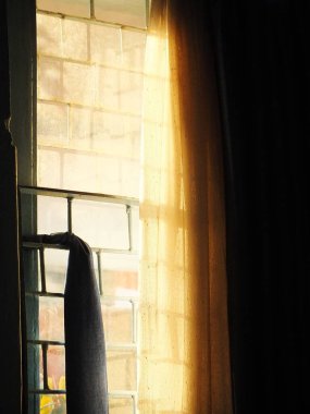 İçerideki odadan dışarı bakan, perdeli bir pencereden bakan. Yanından geçen güneş ışığı huzur ve yalnızlık ortamı yaratıyor.