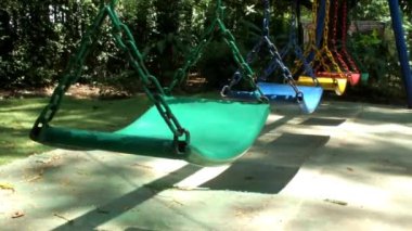 Güneşli bir günde, açık hava parkındaki çocuk parkında rüzgarda savrulan boş bir salıncakla ortam rahatlatıcı.