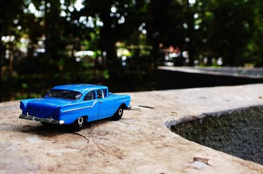 Mavi oyuncak araba çimento yüzeyinde. Araba küçük ve ona klasik bir görünümü var. Sahne huzurlu ve sakin, resimdeki tek nesne araba.