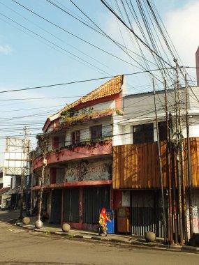 Bandung City, Batı Java, Endonezya, 25 Ocak 2025. Kırmızılı kadın kırmızı çatılı bir binanın önünde yürüyor. Karmaşık elektrik kablolarını görebilirsiniz.