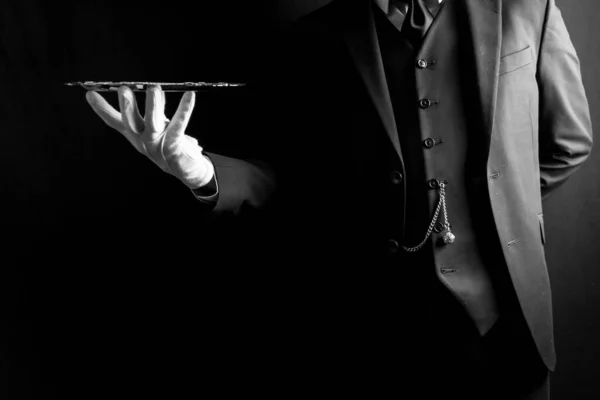 Portrait of Butler or Waiter in Dark Suit and White Gloves Expertly Holding Silver Tray on Black Background. Concept of Service Industry and Professional Hospitality.