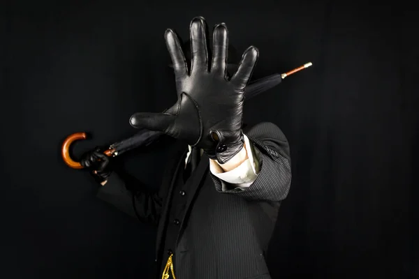 Gentleman in Dark Suit and Leather Gloves with Hand Open on Black Background. Concept of Classic and Eccentric British Gentleman Stereotype. Film Noir Spy Hero Secret Agent
