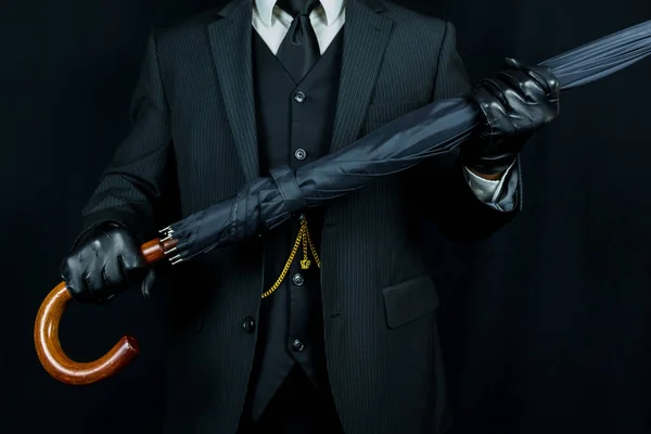 Gentleman in Dark Suit Holding Umbrella on Black Background. Concept of Classic and Eccentric English Gentleman Stereotype. Film Noir Spy Hero