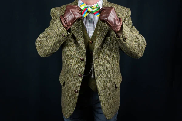 Gentleman in Tweed Suit and Leather Gloves Straightening Bow Tie on Black Background. Concept of Classic and Eccentric British Gentleman