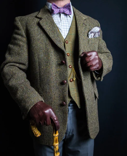 Portrait of Man in Tweed Suit and Leather Gloves Holding Umbrella on Black Background. Classic and Eccentric English Gentleman.