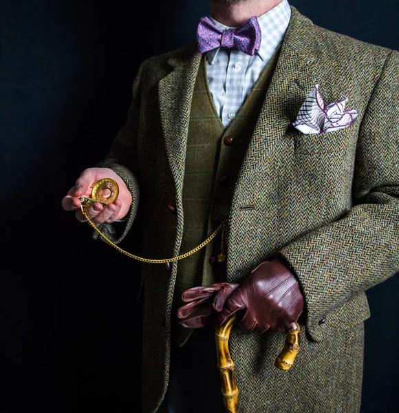 Portrait of British Gentleman in Tweed Suit and Leather Gloves Holding Gold Pocket Watch on Black Background. Retro Style and Vintage Fashion.