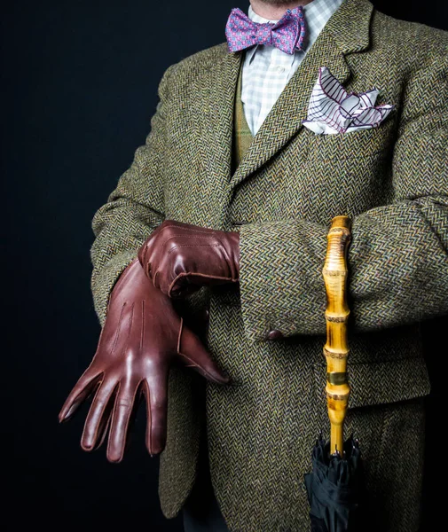 Portrait of Man in Tweed Suit Pulling on Leather Gloves on Black Background. Vintage Style and Retro Fashion of British Gentleman