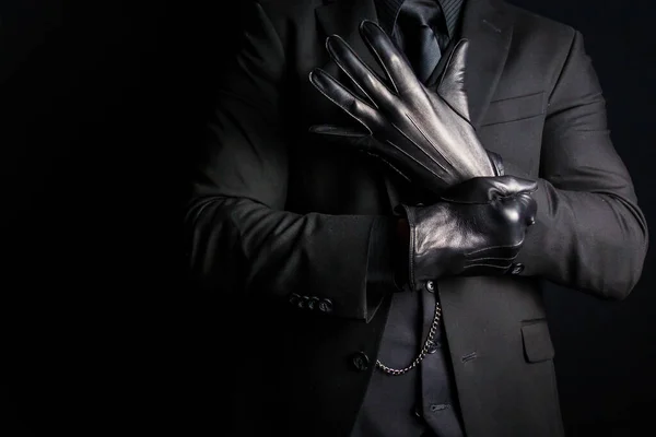 Portrait of Strong Man in Dark Suit Pulling on Black Leather Gloves. Dark Criminal Activity. Threat of Dangerous Violence